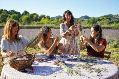 Quatre participantes autour d'une table pour un atelier de création de fuseaux de lavande devant un champ de lavande - Agrandir l'image 20 sur 25, fenêtre modale